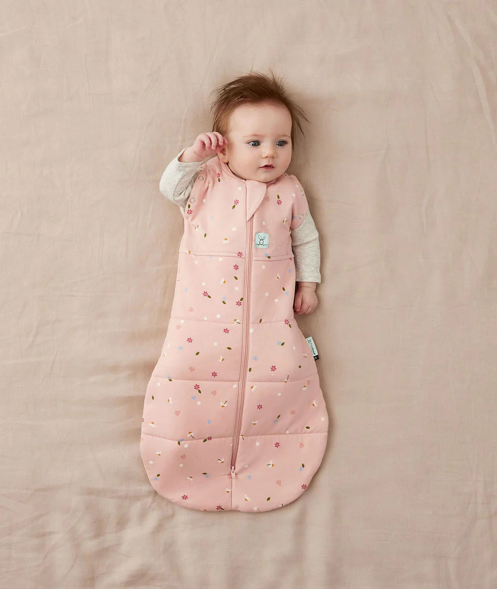 Baby lying on a pink blanket wearing a pink patterned sleeping bag.