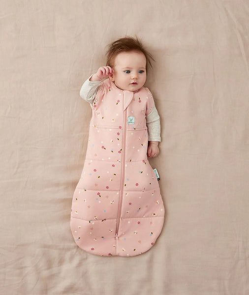 Baby lying on a pink blanket wearing a pink patterned sleeping bag.