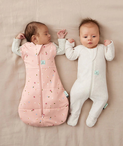 Two babies wearing sleeping bags on a beige surface