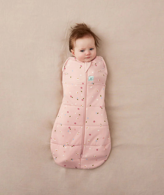 Baby lying on a beige surface wearing a pink sleeping bag with floral pattern