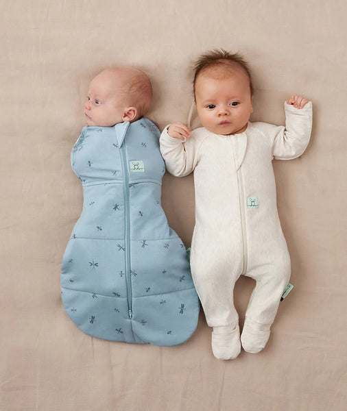 Two babies wearing blue and white sleep sacks on a beige surface