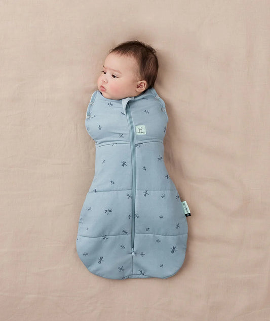 Baby wrapped in a blue sleeping bag on a beige surface