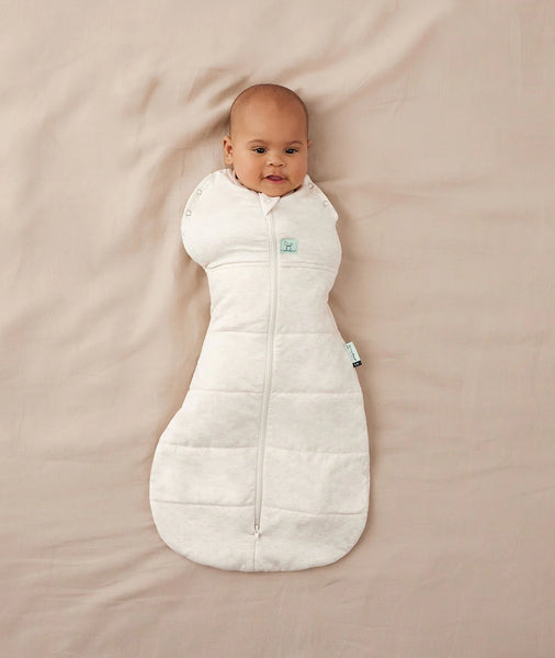 Baby wrapped in a white sleeping bag on a beige blanket
