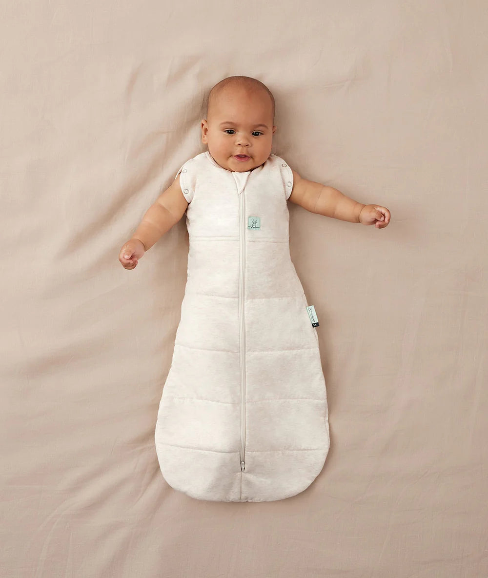 Baby lying on a beige blanket wearing a white sleeping bag