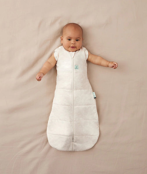 Baby lying on a beige blanket wearing a white sleeping bag