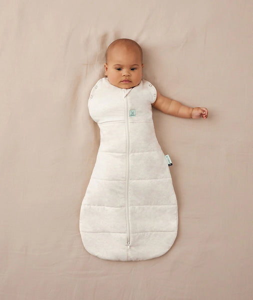 Baby lying in a white sleeping bag on a beige blanket
