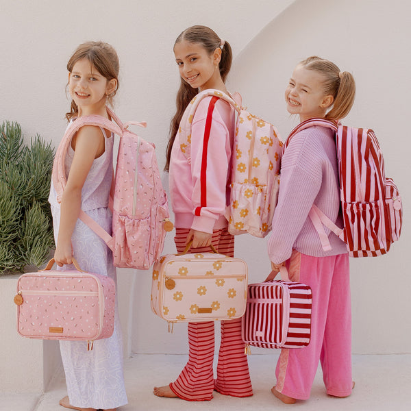 Three young girls with colorful backpacks and lunch bags in a bright setting