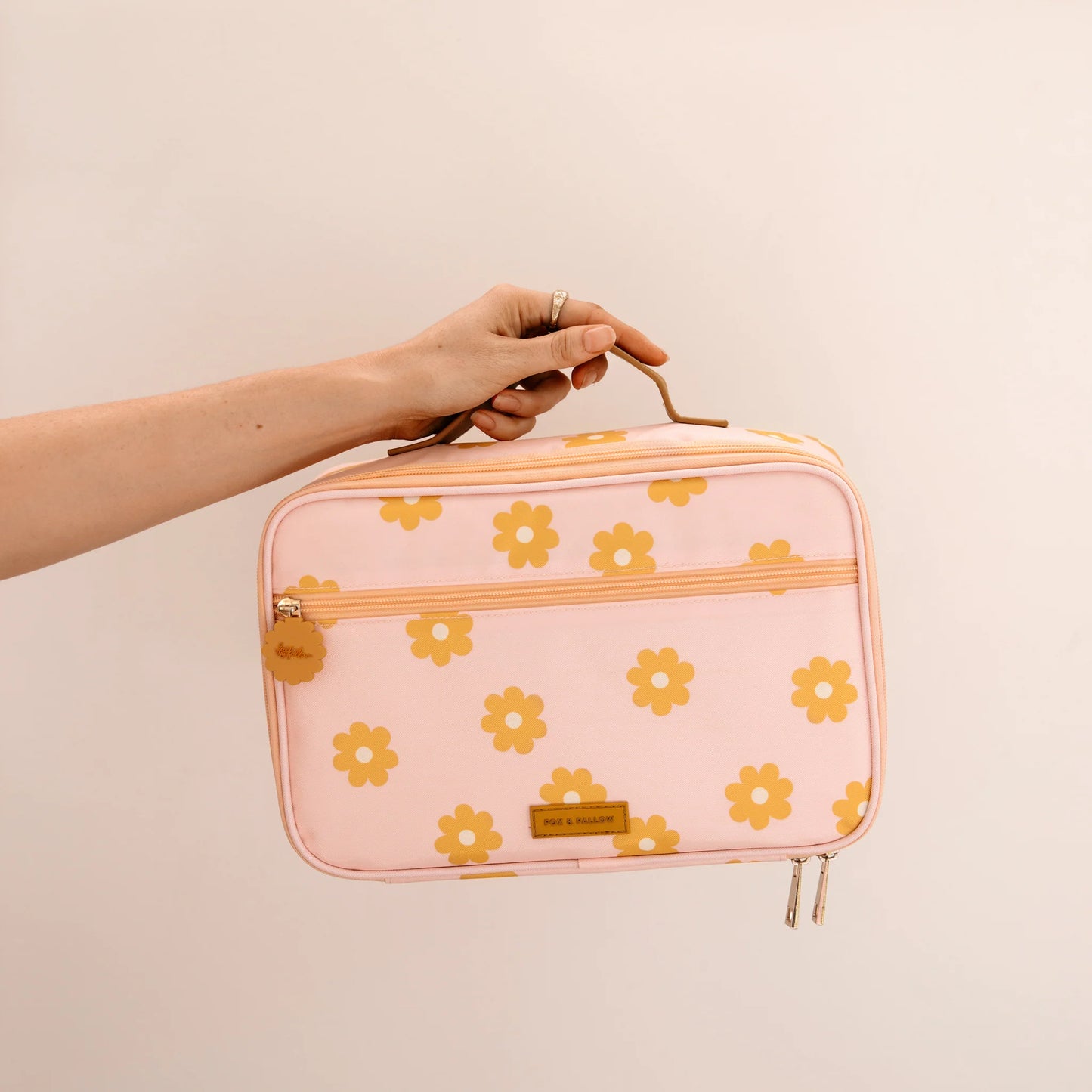Pink lunch case with yellow floral pattern held by a hand against a beige background