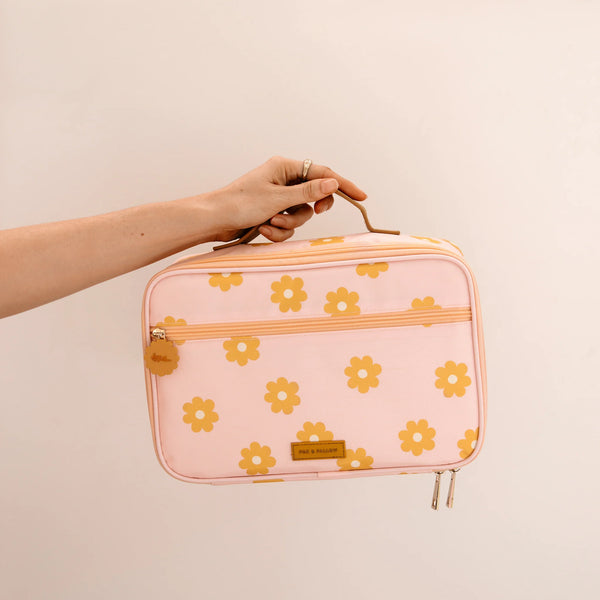 Pink lunch case with yellow floral pattern held by a hand against a beige background