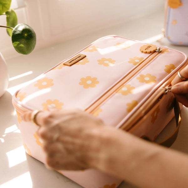 Pink floral-patterned lunch bag with a hand holding it on a light surface.