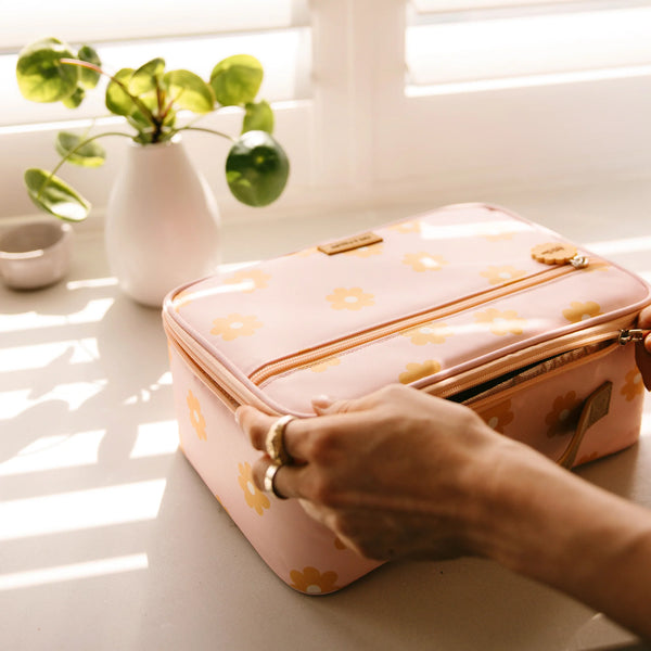 Pink floral-patterned lunch bag being held on a light surface with plants in the background