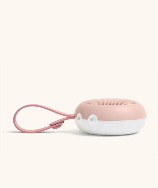 Pink and white portable speaker with a strap on a light gray background