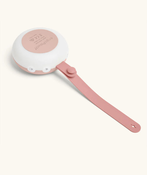 Small pink white noise machine with a white handle on a light beige background