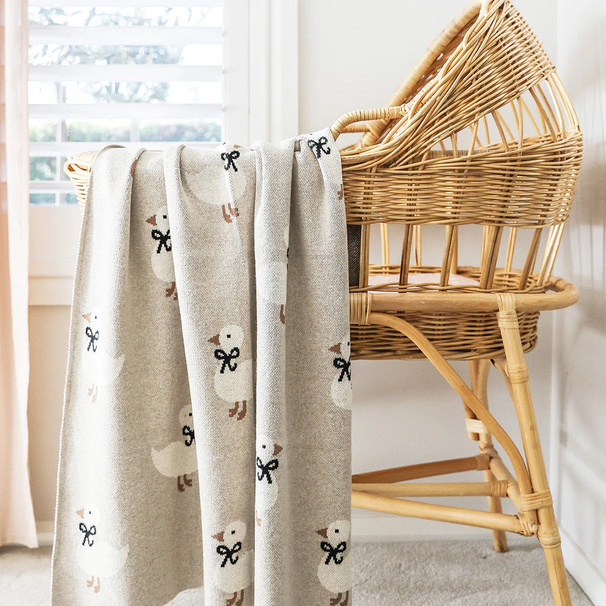 Textured blanket with duck pattern draped over a wicker chair in a bright room.