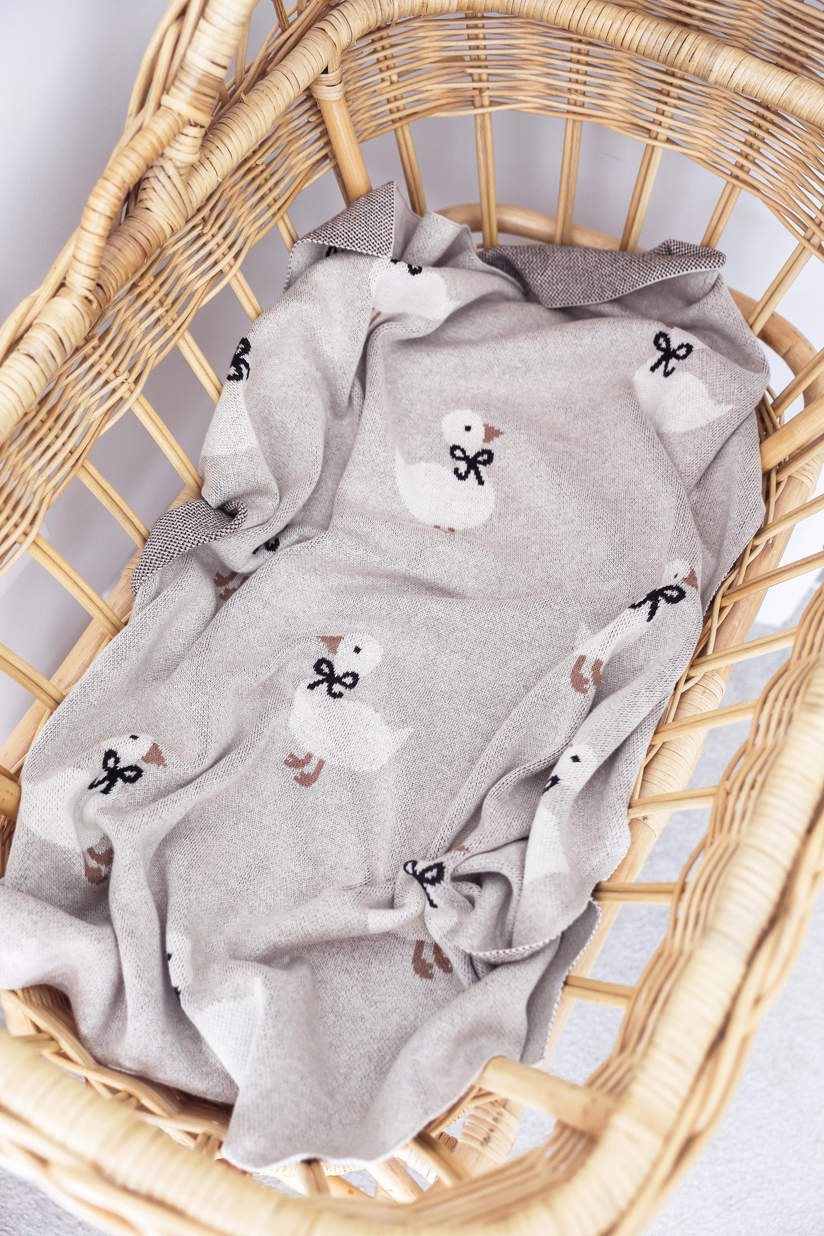 Gray baby blanket with duck pattern in a wicker basket