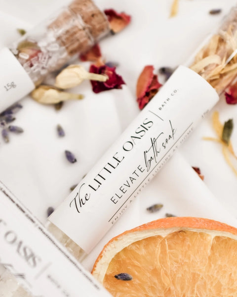 Bath soap bars with 'The Little Oasis' and 'Elevate Bath Soap' text, surrounded by dried flowers and fruits.