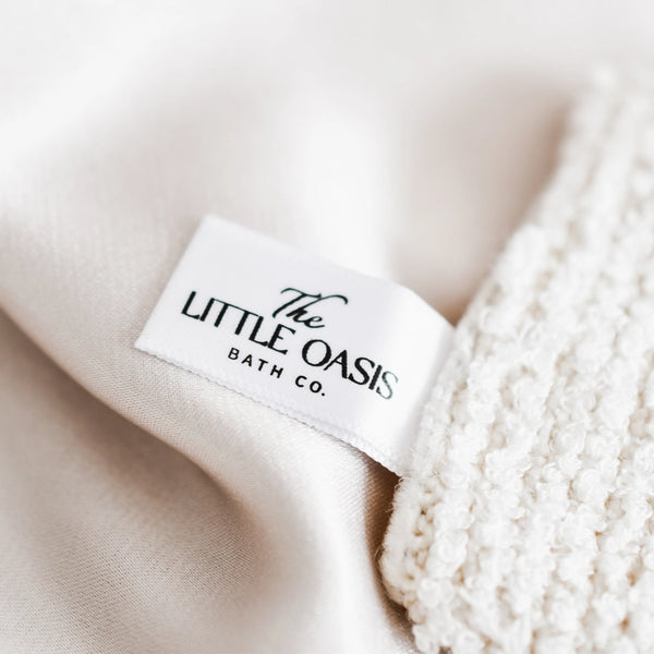 Label of The Little Oasis Bath Co. on a textured beige fabric background