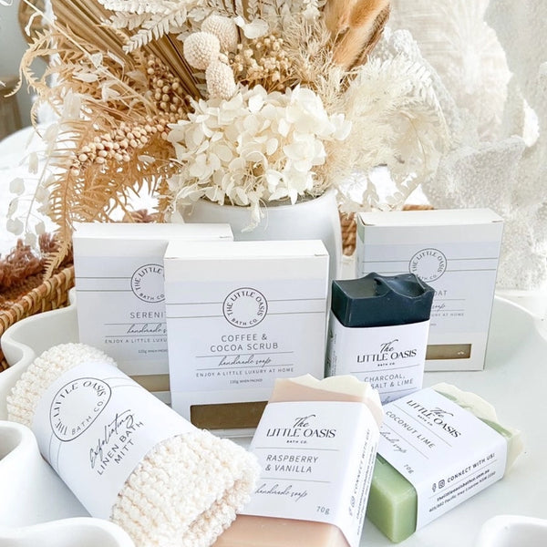 Collection of bath products including soaps and scrubs with 'The Little Oasis' branding on a neutral background.
