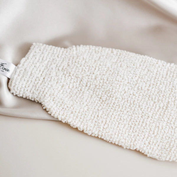 White textured bath mitt on a white surface with 'The Oasis' label.