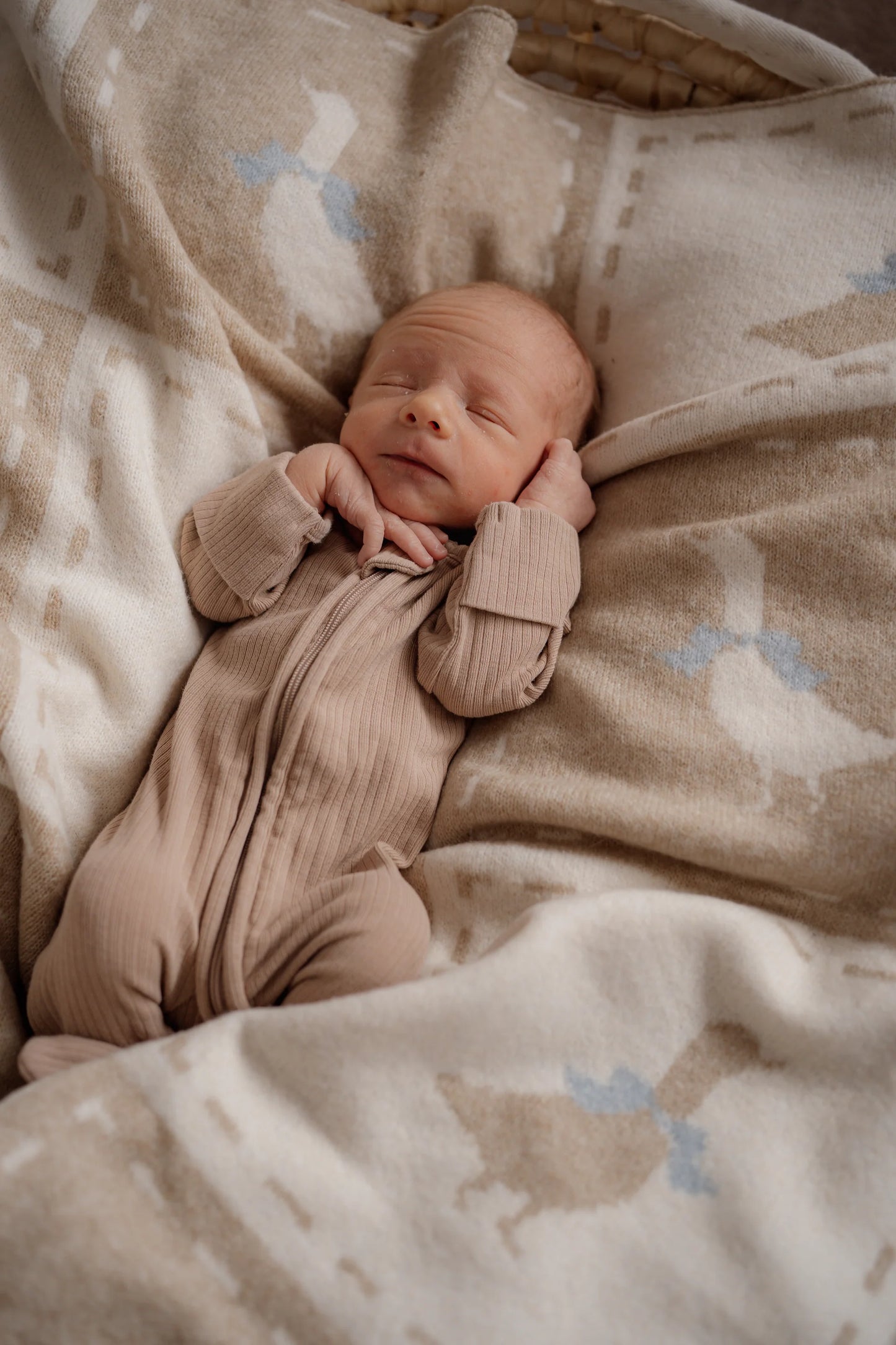 Newborn baby in a pink outfit lying on a patterned blanket