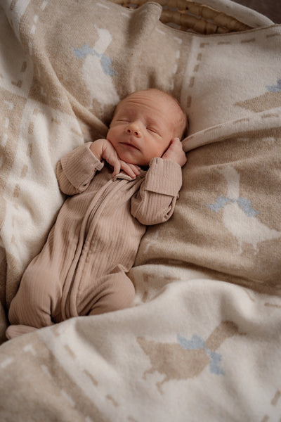 Newborn baby in a pink outfit lying on a patterned blanket