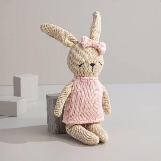 Knitted bunny toy with a pink dress and bow on a light background