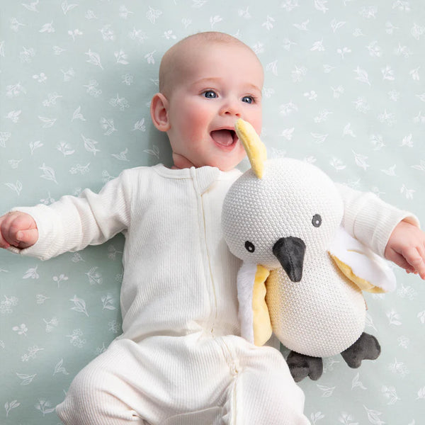 Baby holding a plush toy against a light blue background with subtle patterns