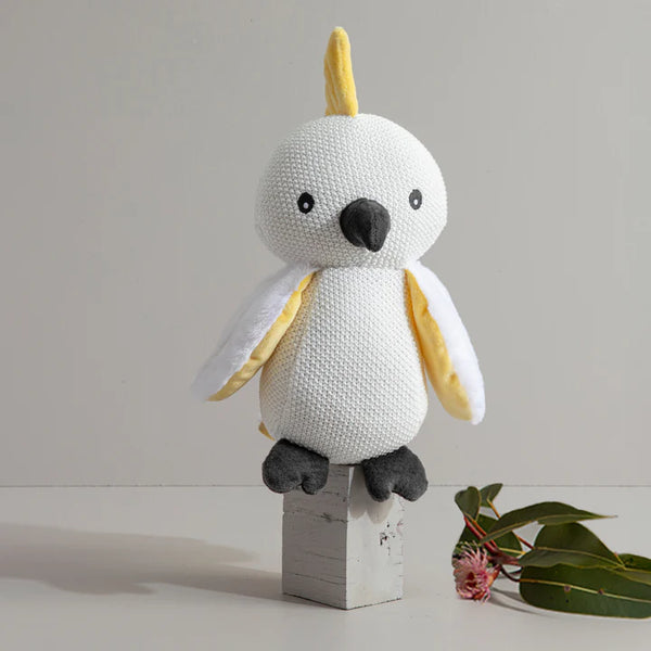 White and yellow stuffed toy on a wooden block with a minimal background