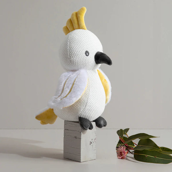 Knitted toy bird with yellow crest on a wooden block against a light background