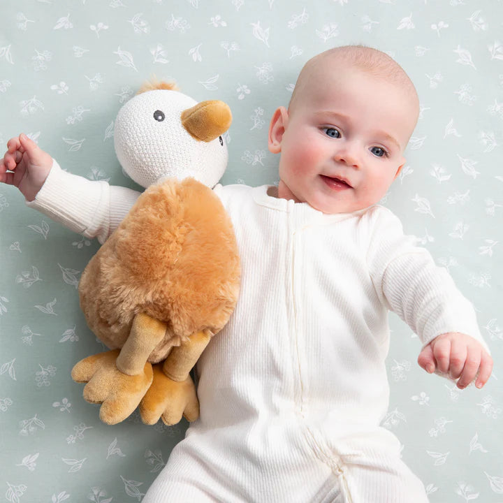 Baby in a white onesie holding a plush duck toy against a light gray background