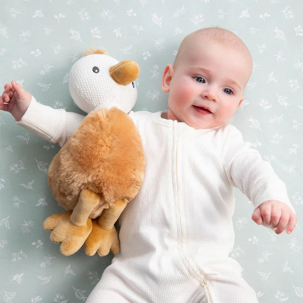 Baby in a white onesie holding a plush duck toy against a light gray background