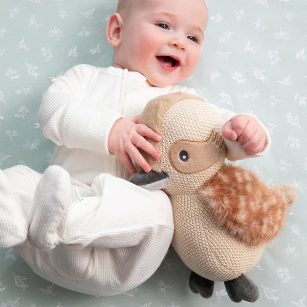 Baby holding a knitted toy with a neutral background