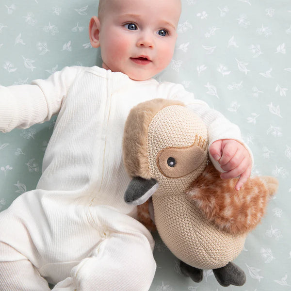 Baby holding a knitted toy duck against a light background