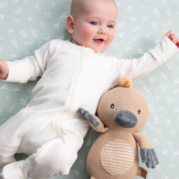 Baby in a white onesie holding a knitted toy against a light gray background