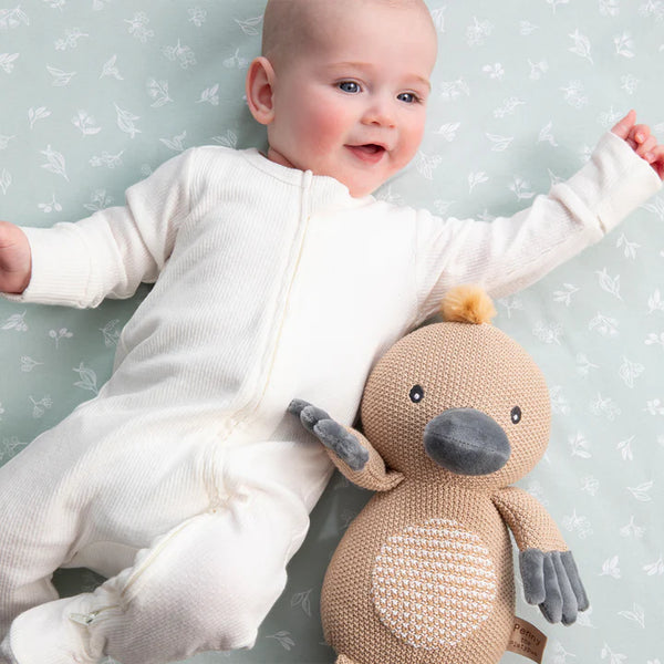 Baby in a white onesie holding a knitted toy against a light gray background