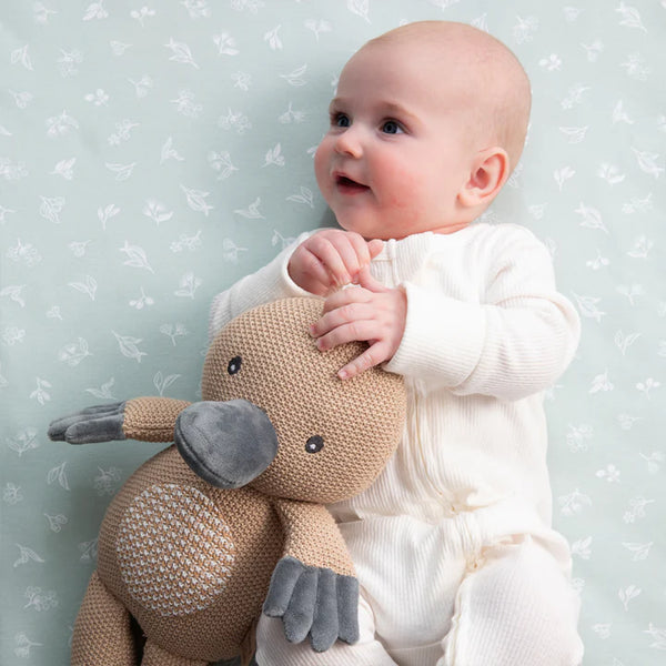 Baby holding a knitted toy against a light blue floral-patterned background