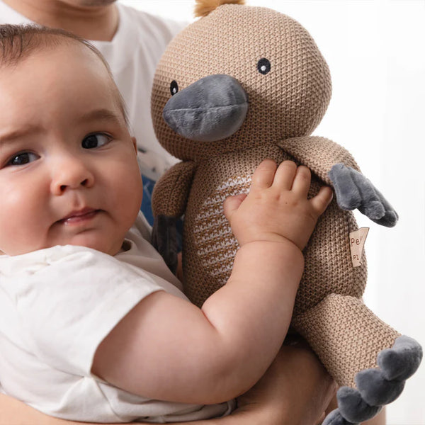 Baby holding a knitted toy with a neutral background