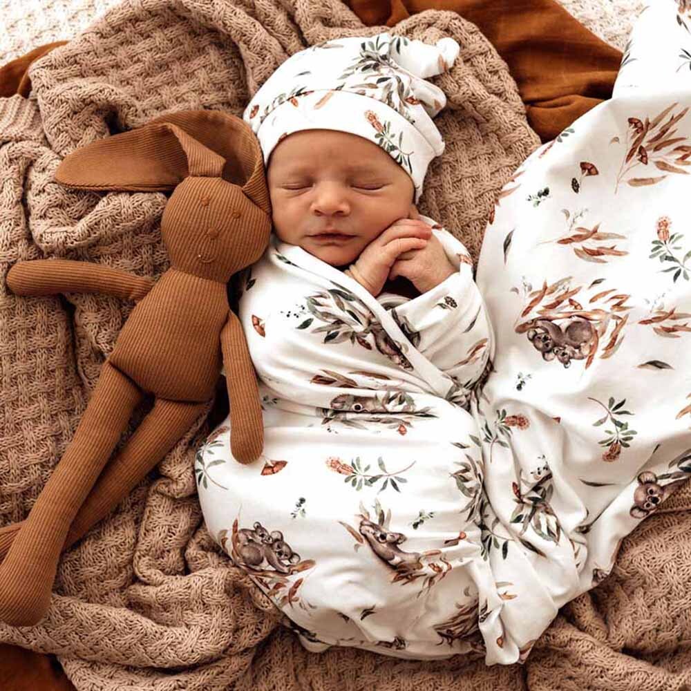 Newborn baby wrapped in a floral patterned blanket with a brown stuffed toy on a soft surface.