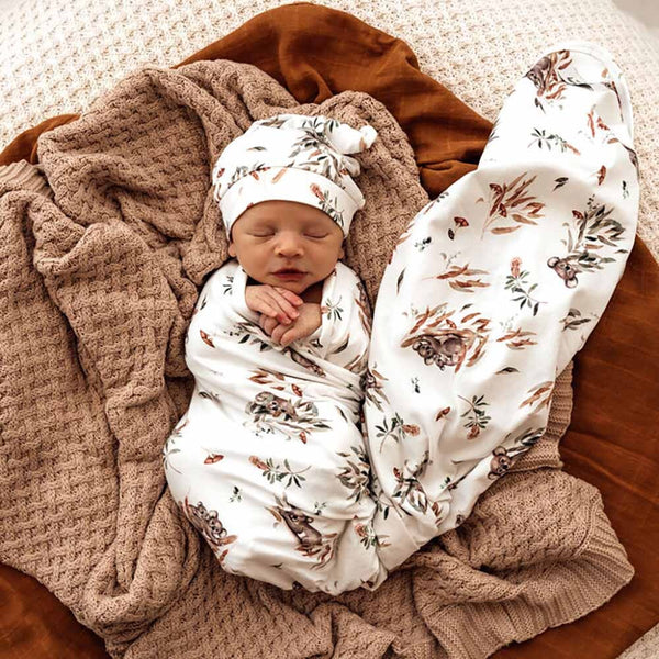 Newborn baby swaddled in a floral blanket with a matching hat on a soft surface.