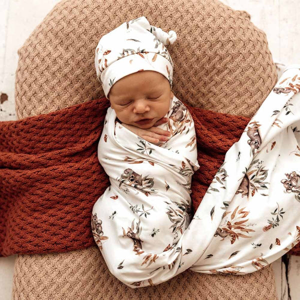 Newborn baby swaddled in a floral pattern with a matching headband, lying on a textured surface.