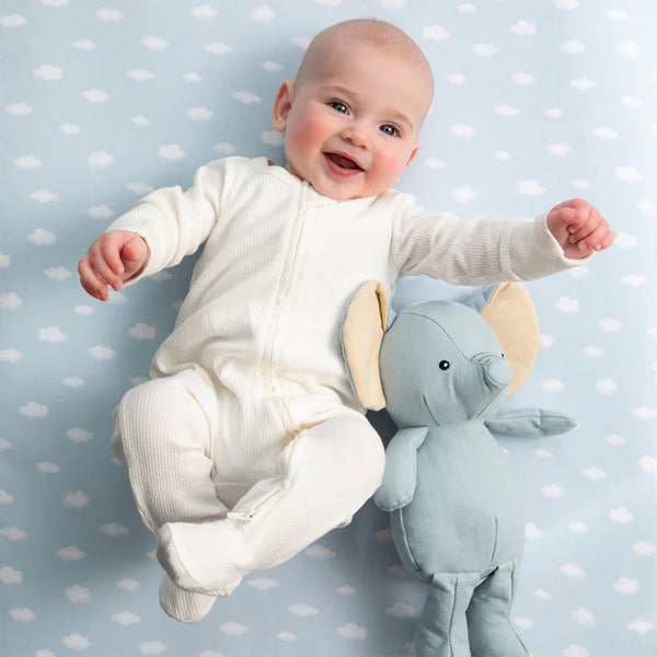 Baby in a white onesie with a plush elephant toy on a polka dot background