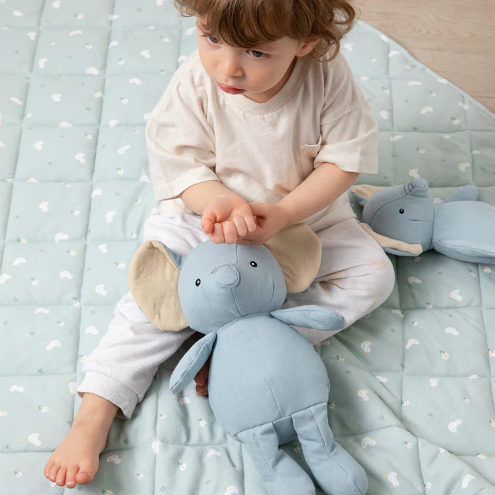 Child holding a blue plush elephant toy on a light blue blanket with white patterns