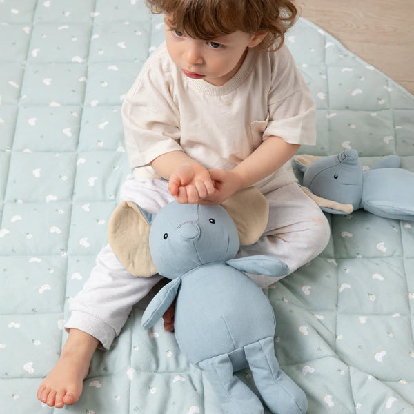 Child holding a blue plush elephant toy on a light blue blanket with white patterns