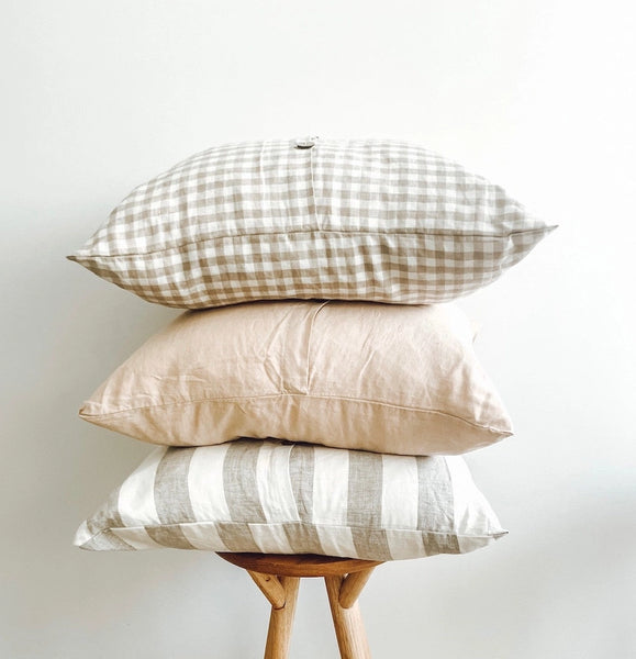 Stack of three pillows with different patterns on a wooden stand against a light background