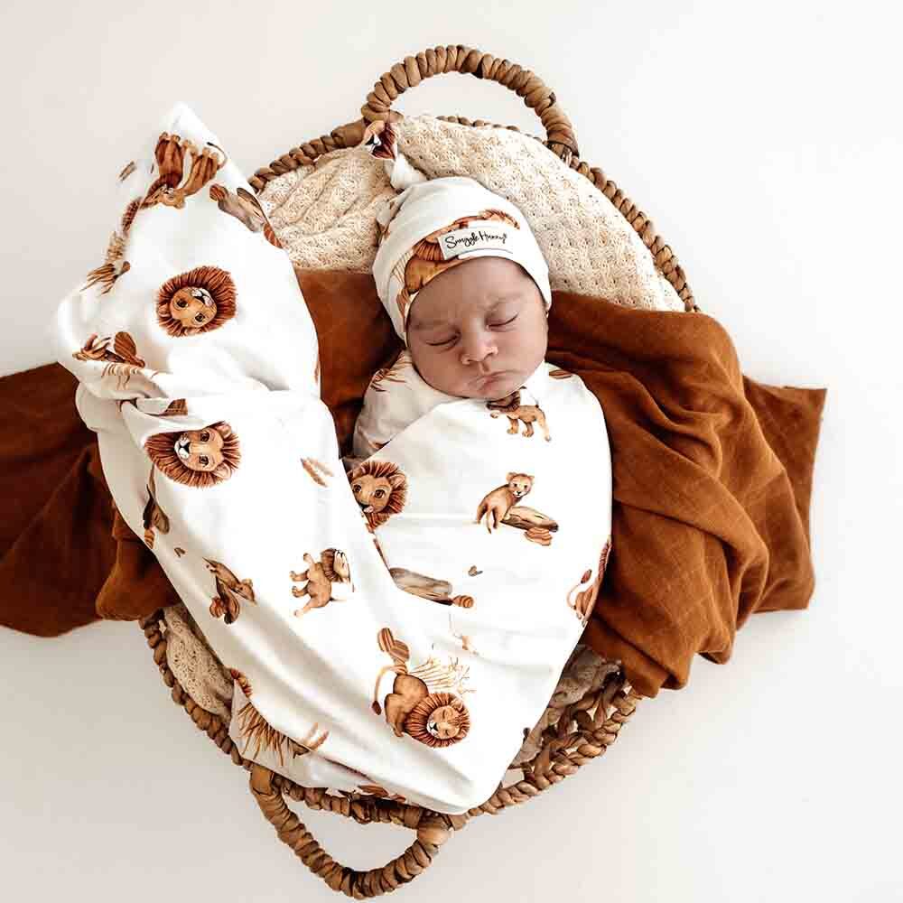 Newborn baby wrapped in a lion-patterned swaddle blanket and hat, lying in a woven basket.