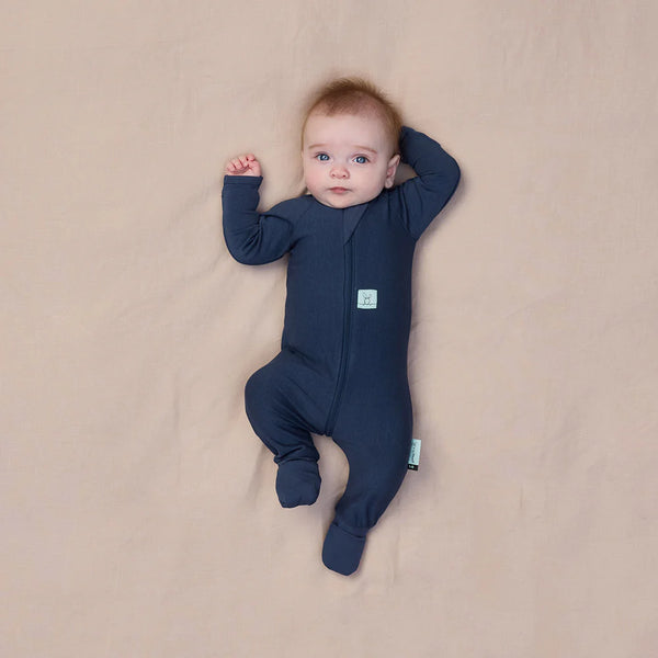 Baby wearing a navy blue onesie lying on a beige surface
