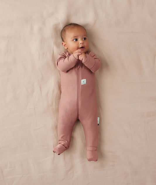 Baby wearing a pink onesie on a beige blanket