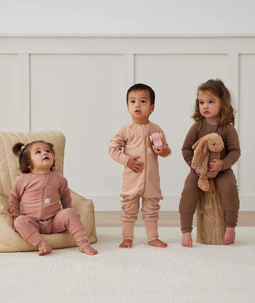 Three children in matching outfits standing in a room with a neutral color palette.