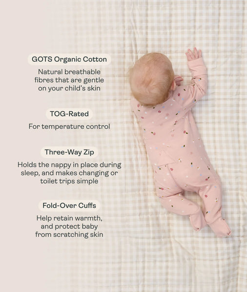 Baby in a pink organic cotton onesie on a checkered blanket with text about its features.