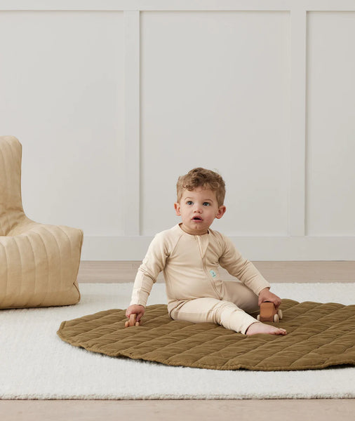 Child sitting on a textured rug in a minimalistic room with a beige chair.
